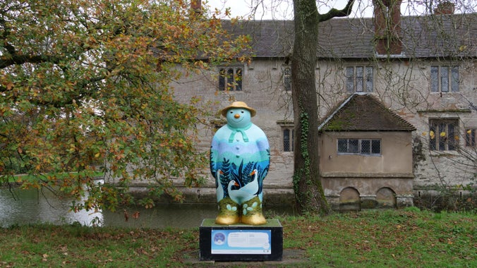 A statue of the Snowman™ coloured blue with geese on its front pictured outside Baddesley Clinton, Warwickshire.